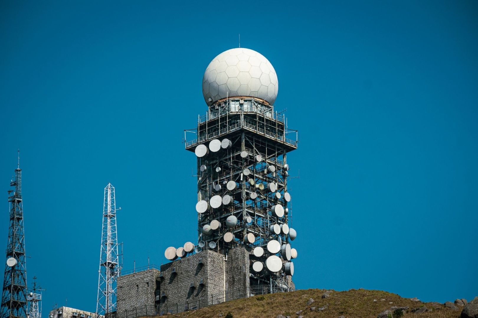 Radiotorn med parabolantenner och stor radom mot klarblå himmel